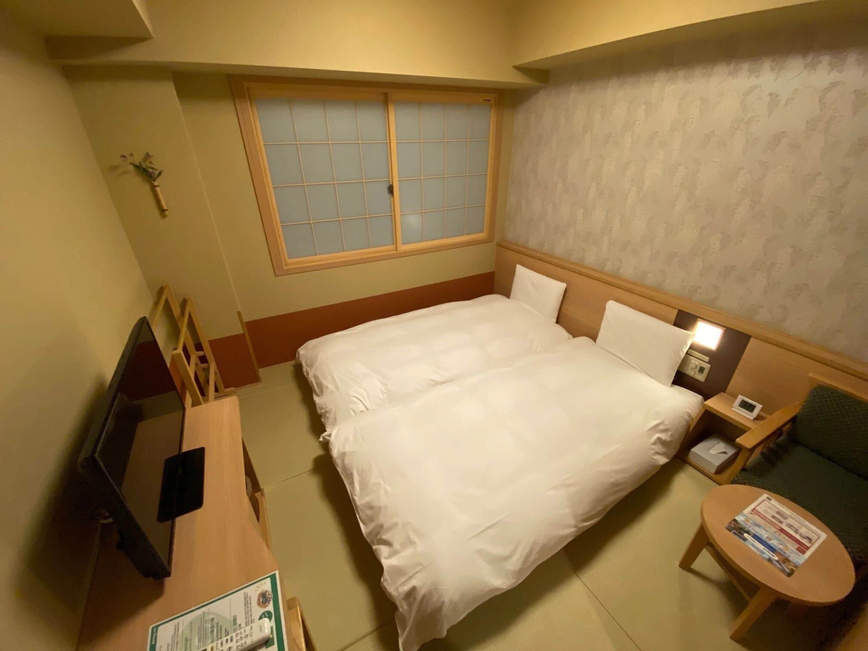 A hotel room with a bed, bedside tables, a television, a window, and a small table with a magazine.