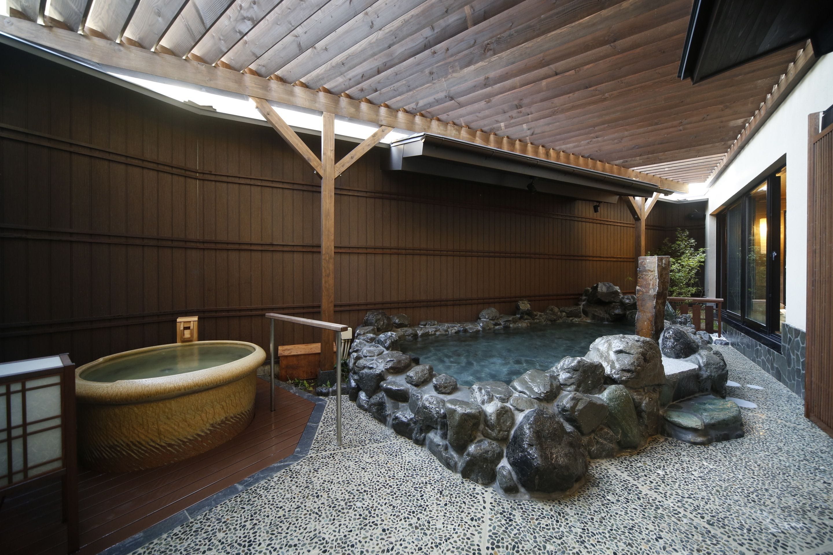 A hot spring area with a large stone bath, wooden beams, and a tiled floor.