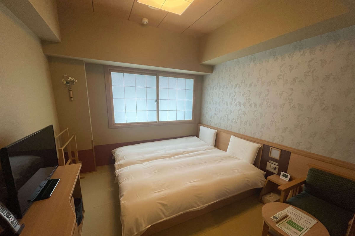 A hotel room with a bed, a TV, a small table, and a window.