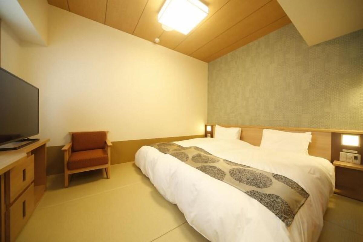 A hotel room with a bed, a television, a chair, and a nightstand.