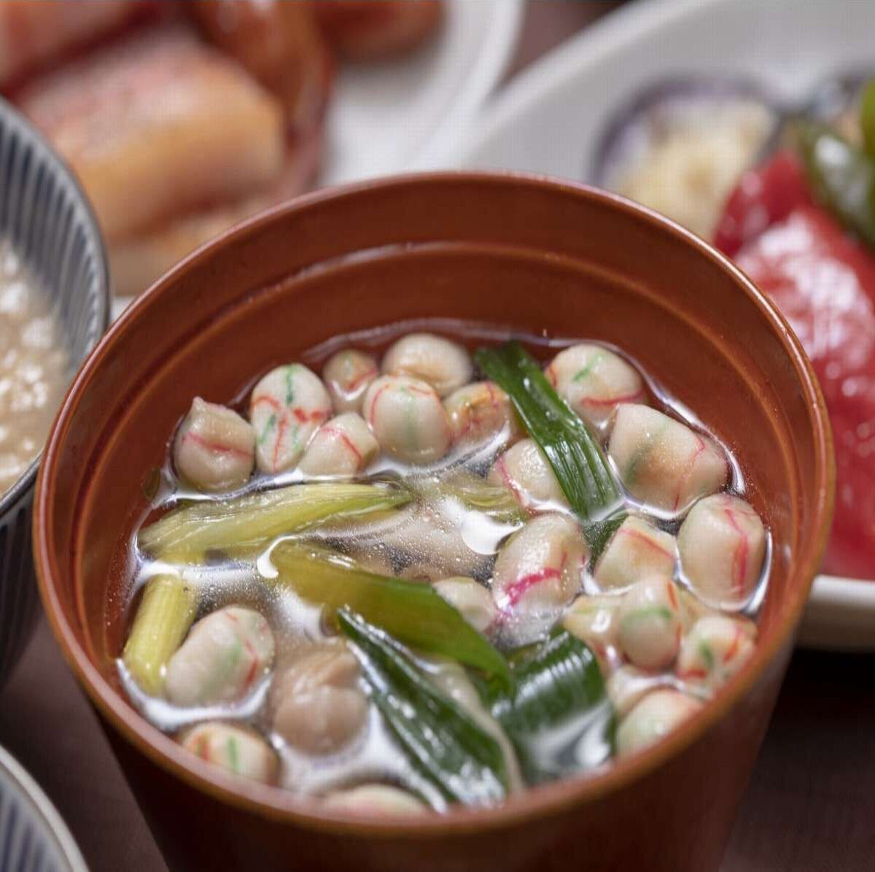 A bowl of soup with round dumplings and green vegetables.