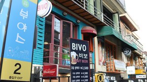 A building with a BIVO Draft Beer sign, a Budweiser refrigerator, and a '2' exit sign. - Housetay Guesthouse 2nd Branch - Hostel (Seoul)