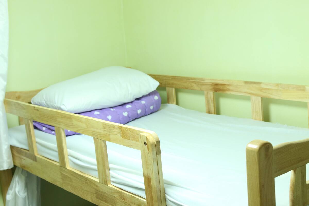 Ein einzelnes Holz Etagenbett mit einer weißen Matratze und einem Kissen in Lila mit weißen Herzmustern.