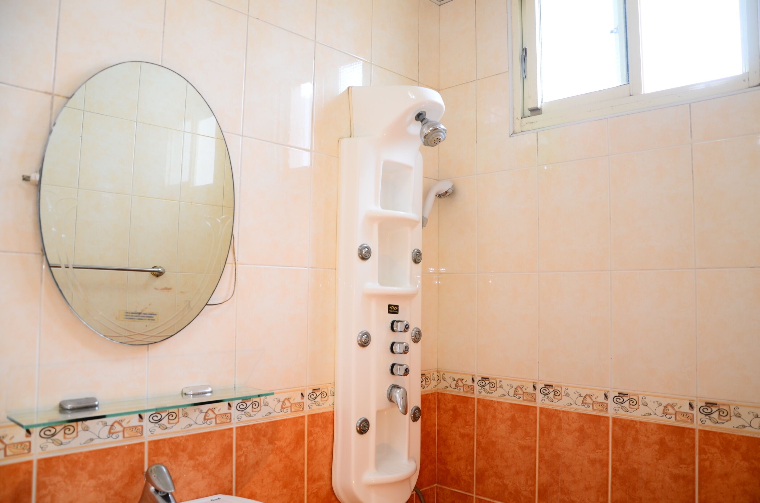 A bathroom with a glass shower enclosure, a round mirror, and decorative tiles.