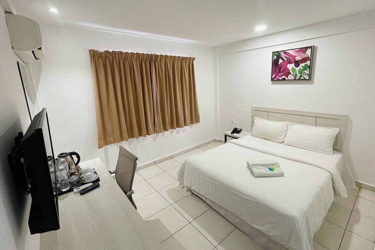 Une chambre d’hôtel comprenant un lit, un bureau avec une chaise, une télévision et une fenêtre avec des rideaux.