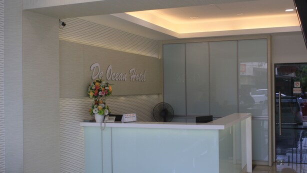 Un comptoir d’accueil avec une pancarte indiquant « De Ocean Hotel », un vase de fleurs et un ventilateur.