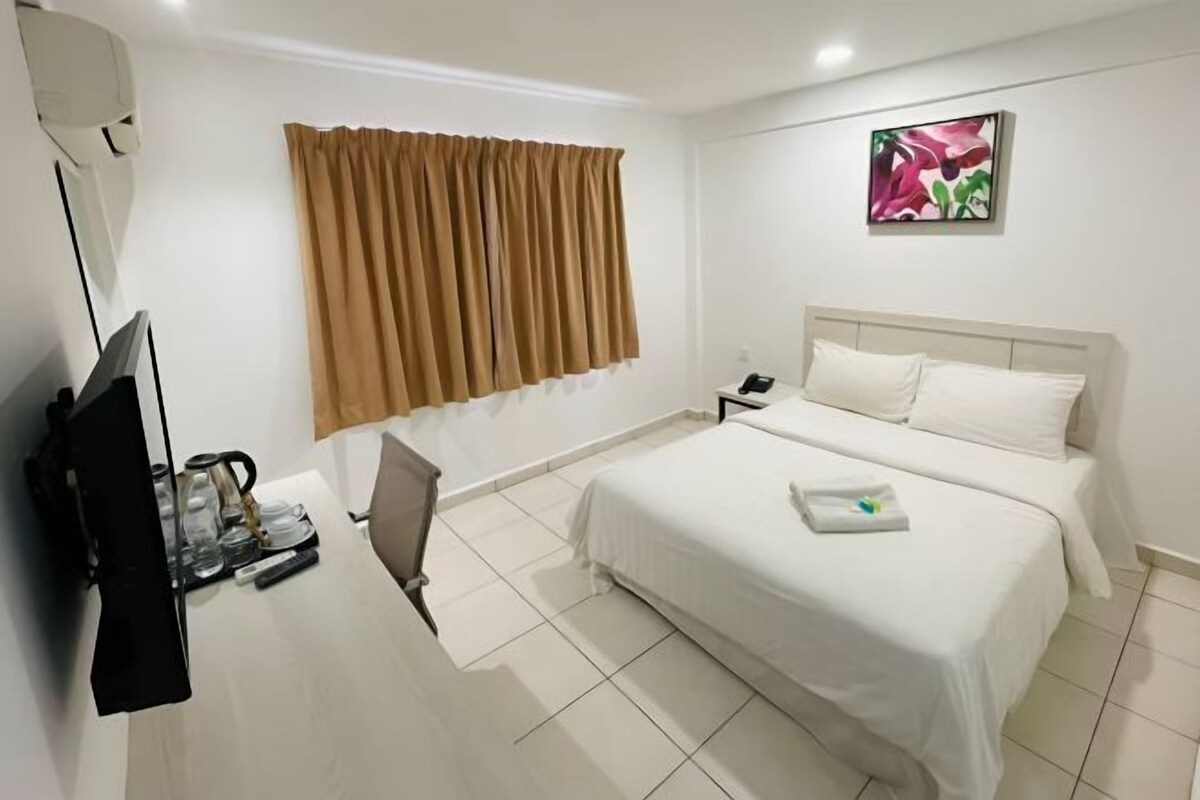 Una habitación de hotel con cama, escritorio con silla, televisión y ventana con cortinas.