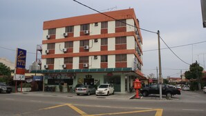 Un hôtel à plusieurs étages, doté d’un auvent vert, avec plusieurs voitures garées devant et une enseigne bien visible indiquant la présence d’un parking.