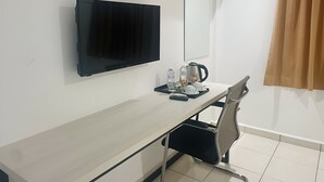 Une chambre d’hôtel équipée d’une télévision à écran plat, d’un bureau avec une machine à café, d’une chaise et d’une fenêtre avec des rideaux.