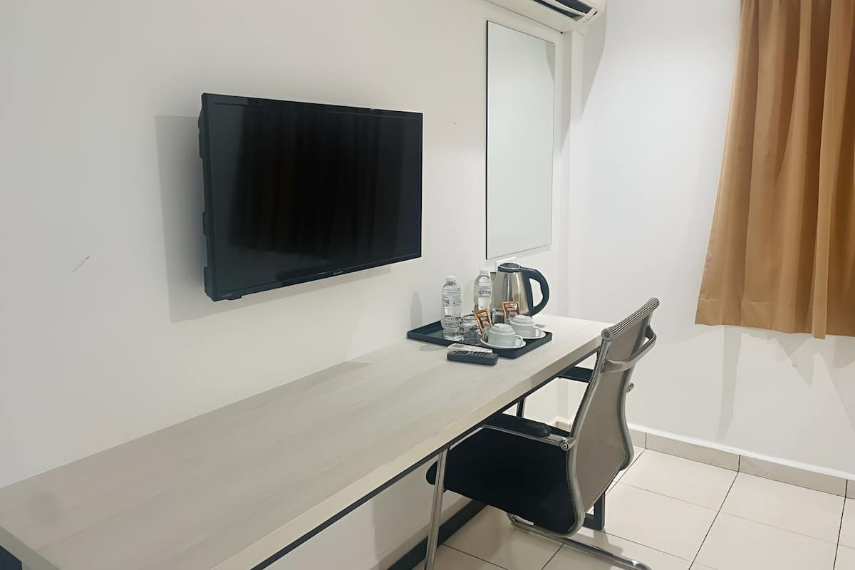 Une chambre d’hôtel équipée d’une télévision à écran plat, d’un bureau avec une machine à café, d’une chaise et d’une fenêtre avec des rideaux.