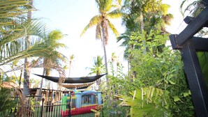 Un área cercada con un colorido parque infantil, rodeada de palmeras y follaje.