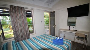 Un dormitorio con cama, escritorio, silla, televisión y ventana con cortinas.