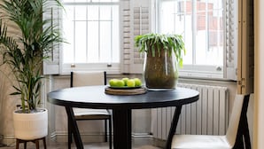 A dining area with a round table, chairs, a potted plant, a vase with green leaves, and a tray of green apples. - GREAT LOCATION -  Luxurious Knightsbridge Apartment - Steps from Harrods (London)