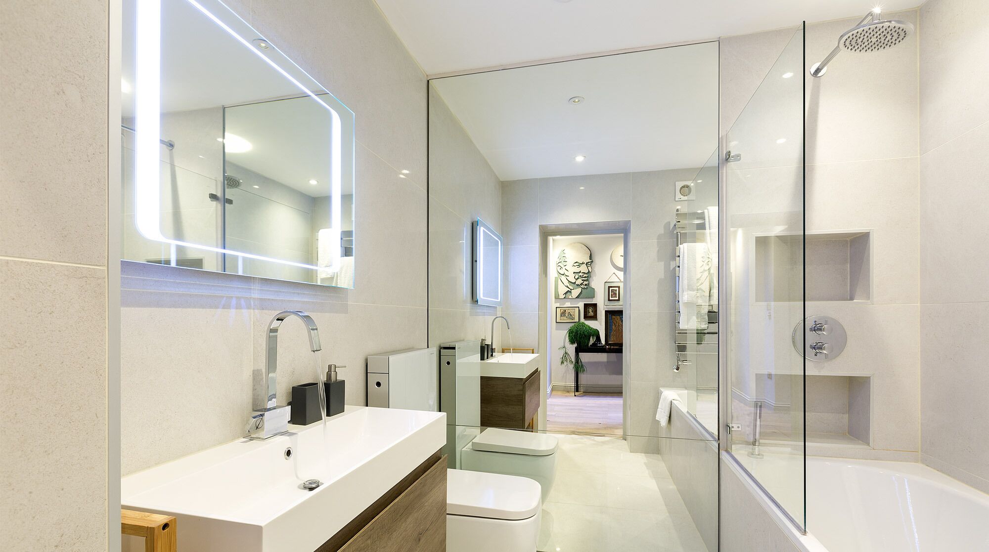 Une salle de bain moderne avec un grand miroir, un lavabo blanc, une douche en verre et des toilettes.