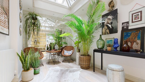 A spacious room with a high ceiling, a dining area with wicker furniture, and various potted plants. - GREAT LOCATION -  Luxurious Knightsbridge Apartment - Steps from Harrods (London)