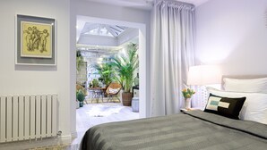 A bedroom with a bed, a nightstand, a lamp, and a window with curtains. There is a framed artwork on the wall and a radiator below the artwork. - GREAT LOCATION -  Luxurious Knightsbridge Apartment - Steps from Harrods (London)