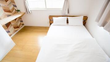Un dormitorio con cabecera de madera, ropa de cama blanca, pared con motivo de espiga y una ventana con cortinas.