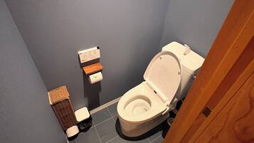 A small bathroom with a toilet, a trash bin, and a pair of slippers on the floor.