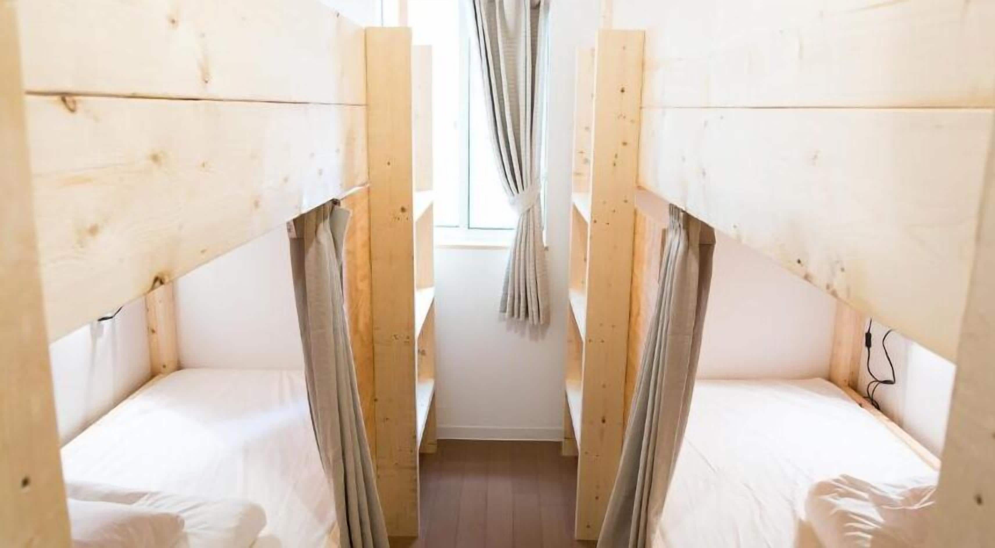 Una habitación estrecha con dos literas, paredes de madera, una ventana con cortinas y suelo de madera.
