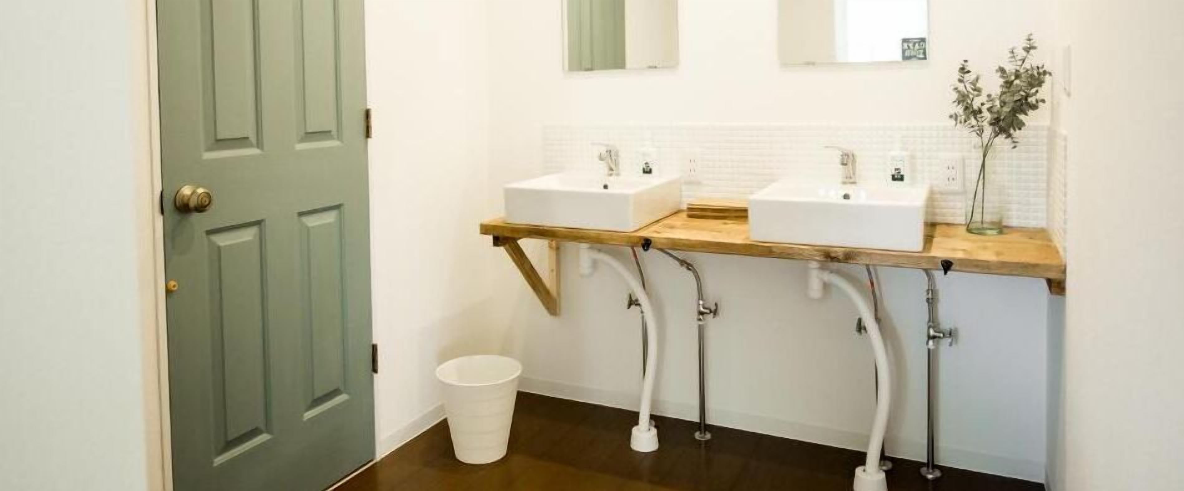 Un baño con dos lavamanos, un mueble de tocador de madera y un cubo blanco.
