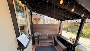 Un espacio al aire libre con un banco de madera, una pequeña mesa y un cartel con la carta.