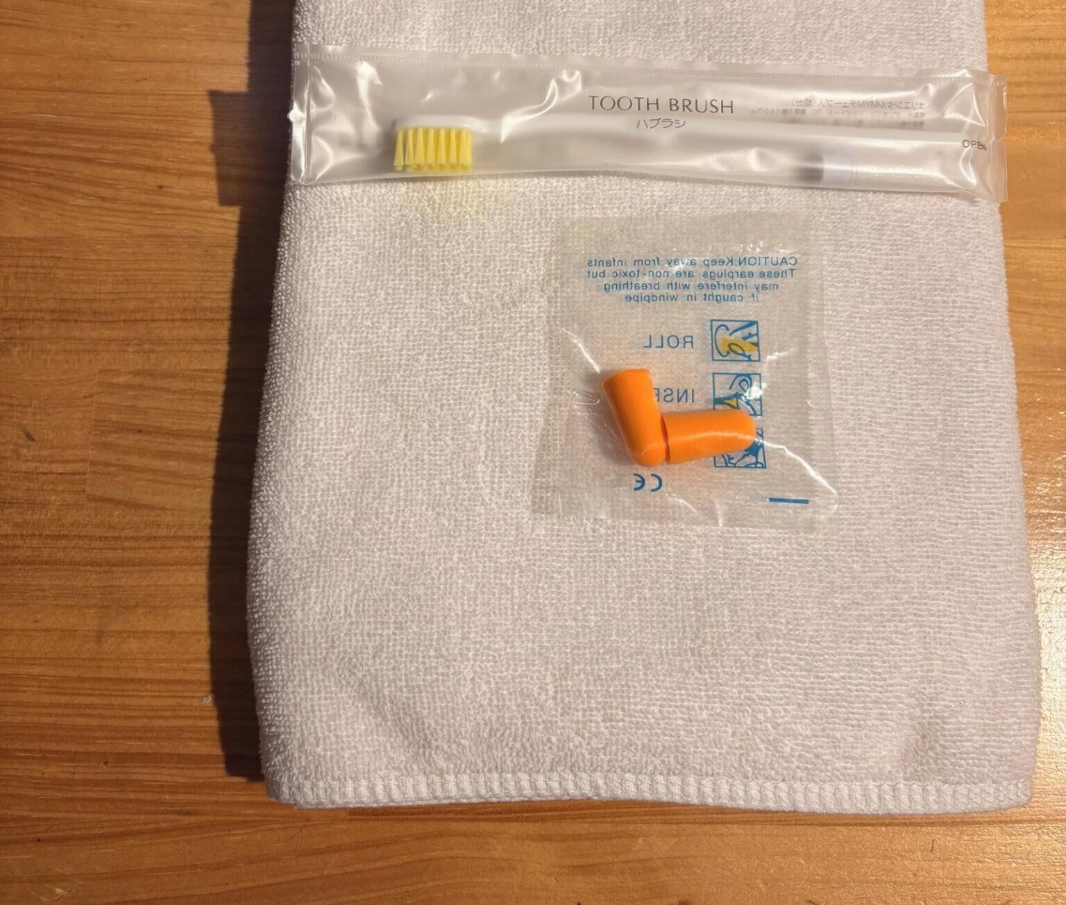 A white towel with a toothbrush and toothpaste in a plastic bag on a wooden surface.
