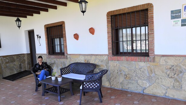 Eine Terrasse mit Steinmauern, zwei Fenster mit Fensterläden, einem Tisch mit Stühlen und einem hängenden Laternen.