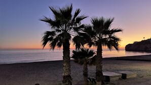 Escena de playa con palmeras y un atardecer.