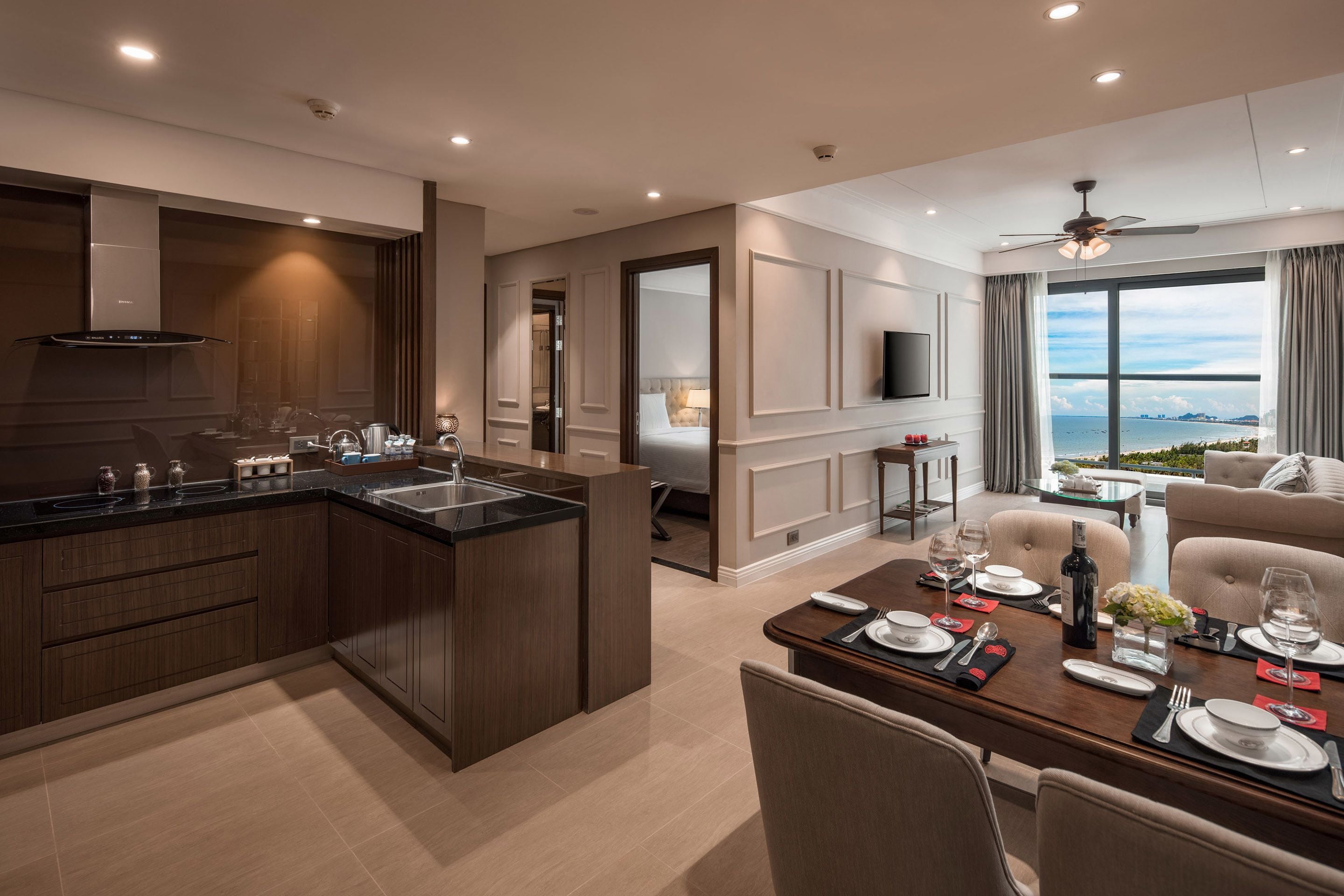 A modern hotel room with a kitchen, dining area, and a balcony with a view.