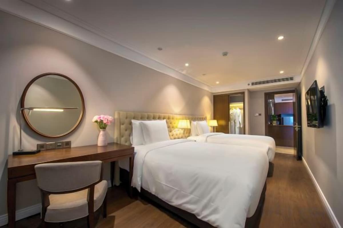 Habitación de hotel con cama, escritorio, silla, espejo redondo y televisor en la pared.
