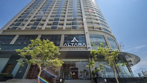 Un grand immeuble d’hôtel au design moderne, avec une enseigne bien visible indiquant « ALTARA SUITES » à l’entrée.