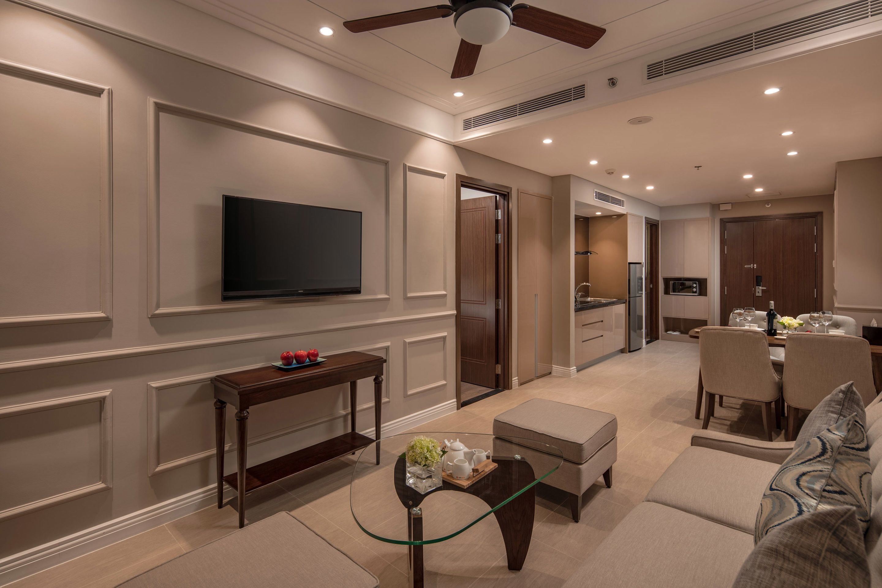 A modern living room with a flat-screen TV, a glass coffee table, a sofa, and a dining area with chairs and a table.