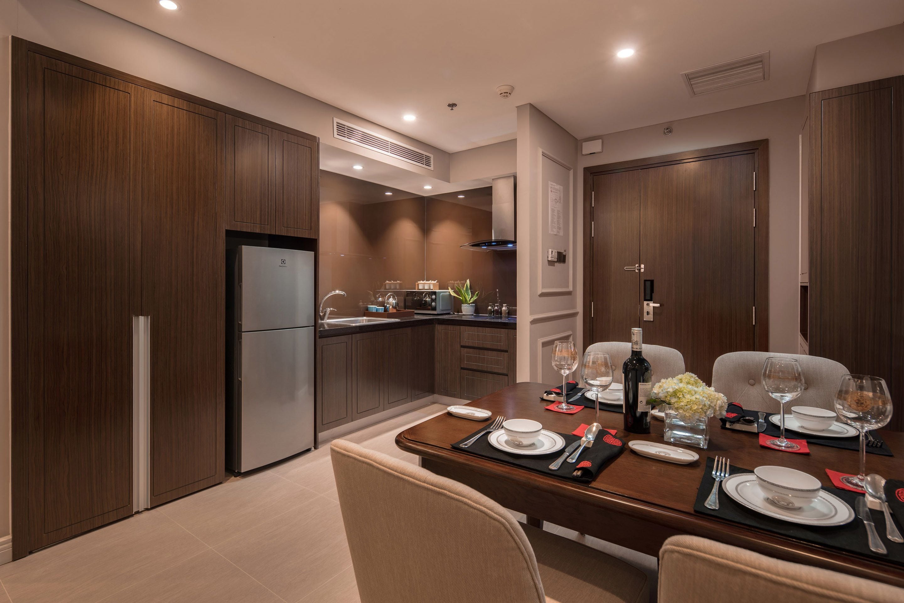 Una cocina moderna con armarios de madera oscura, horno empotrado y comedor con mesa de madera dispuesta para dos personas.