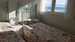 A room with two beds, a window with a view of the sea, and a lamp on a bedside table. - BEAUTIFUL APARTMENT VACATION RENTAL PLAYA SAN JUAN ALICANTE (san juan alicante)