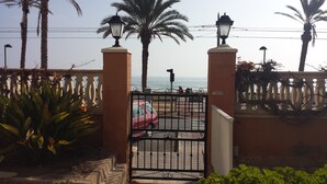 A gated entrance with a red car parked inside, palm trees, and a view of the sea. - BEAUTIFUL APARTMENT VACATION RENTAL PLAYA SAN JUAN ALICANTE (san juan alicante)