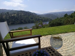 A chair and a table with a glass of wine, overlooking a lake and hills. - Douro Valley With Family (Paços de Gaiolo)