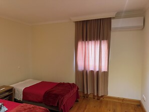 A room with two beds, a wooden floor, an air conditioning unit, and a window with curtains. - Olival House (5-Bedroom) · Douro · Private Pool (Paços de Gaiolo)