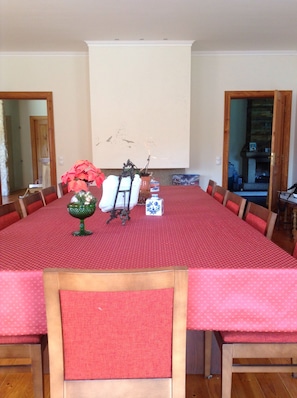 Un coin repas avec une nappe rouge, des chaises en bois, un vase blanc orné de fleurs, un petit bol vert et une boîte blanche à motifs bleus.