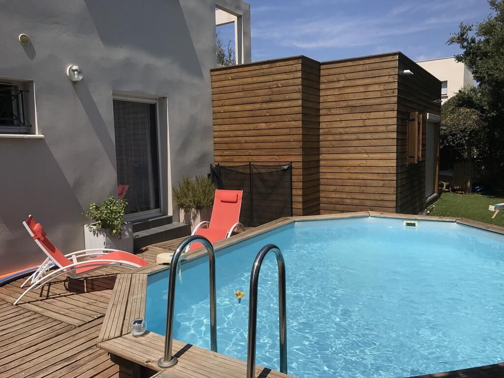 A swimming pool with wooden deck and lounge chairs, surrounded by a modern building with a grey facade.