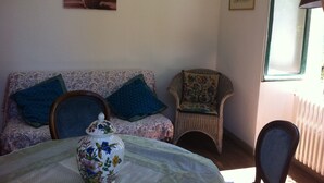 Una habitación con un sofá estampado con motivos florales, una silla de mimbre, un jarrón decorativo y un cuadro en la pared.