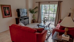 A living room with a red sofa, a TV, a coffee table, and a lamp.