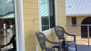 A covered outdoor area with a yellow building, two grey chairs, and a table. - Kozy Kottage on private road. 2 minute walk to private beach.  Pet friendly! (Englewood)