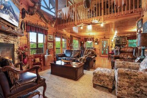 L’intérieur d’une cabane en rondins, avec une cheminée, des meubles en cuir et un balcon orné de bois de cerf.