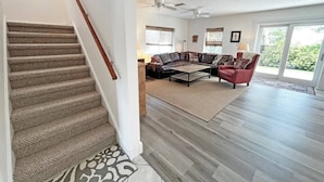 A spacious living room with a large sectional sofa, a red armchair, and a coffee table. There is a staircase with carpeted steps leading to a landing. - Beautiful, well-appointed three-bedroom beach house 300 yards from the beach. (St Augustine)