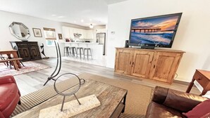 A modern living room with a wooden coffee table, leather sofa, and a large TV mounted on a wooden cabinet. - Beautiful, well-appointed three-bedroom beach house 300 yards from the beach. (St Augustine)