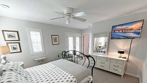 A bedroom with a bed, dresser, mirror, ceiling fan, and artwork on the wall. - Beautiful, well-appointed three-bedroom beach house 300 yards from the beach. (St Augustine)