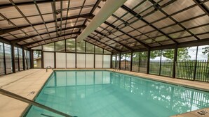Piscina interna com água cristalina, rodeada por área coberta com vigas de metal e painéis de vidro.