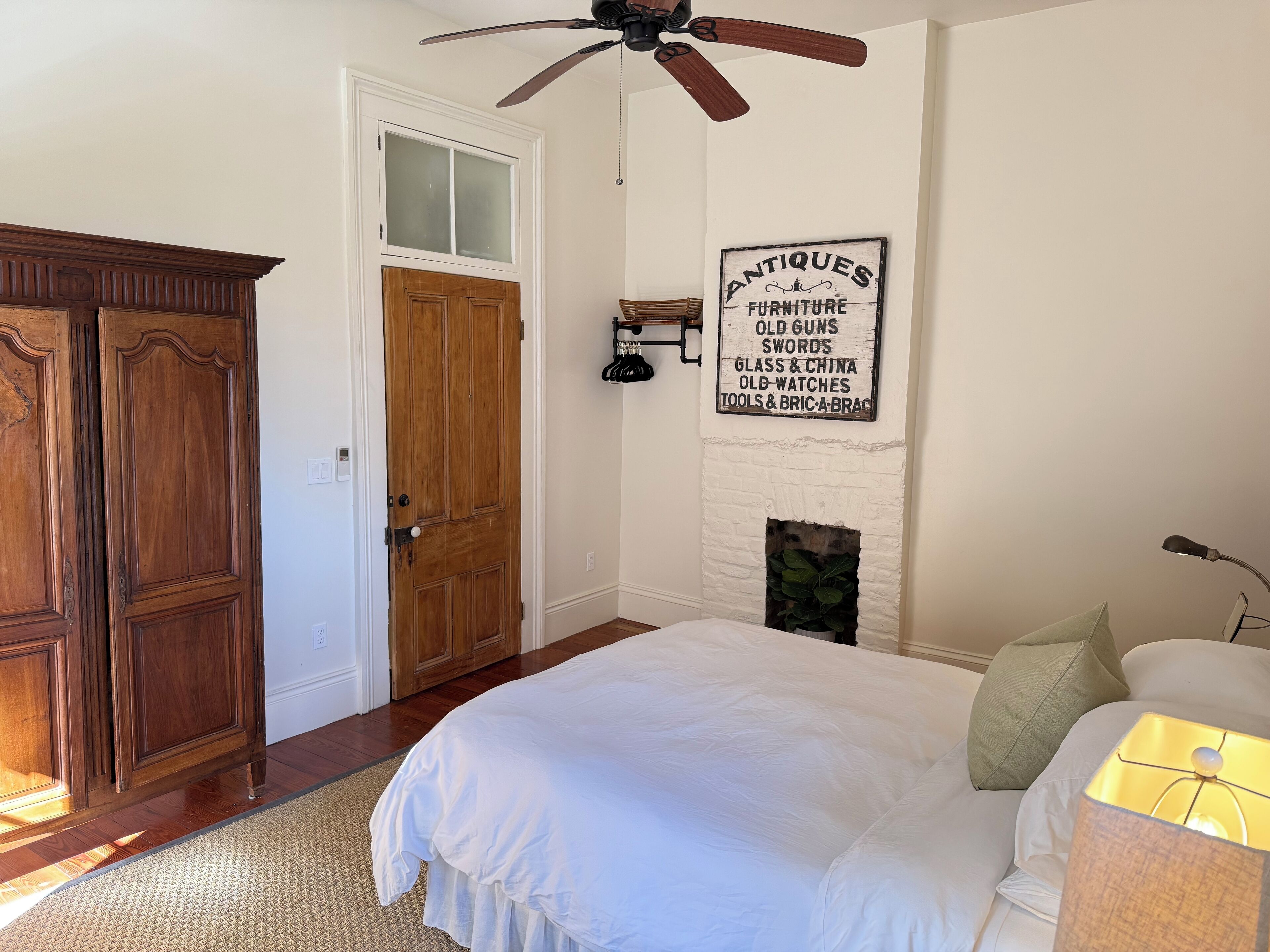 Une chambre avec une armoire en bois, un lit blanc, un panneau fixé au mur indiquant des antiquités, et une cheminée.