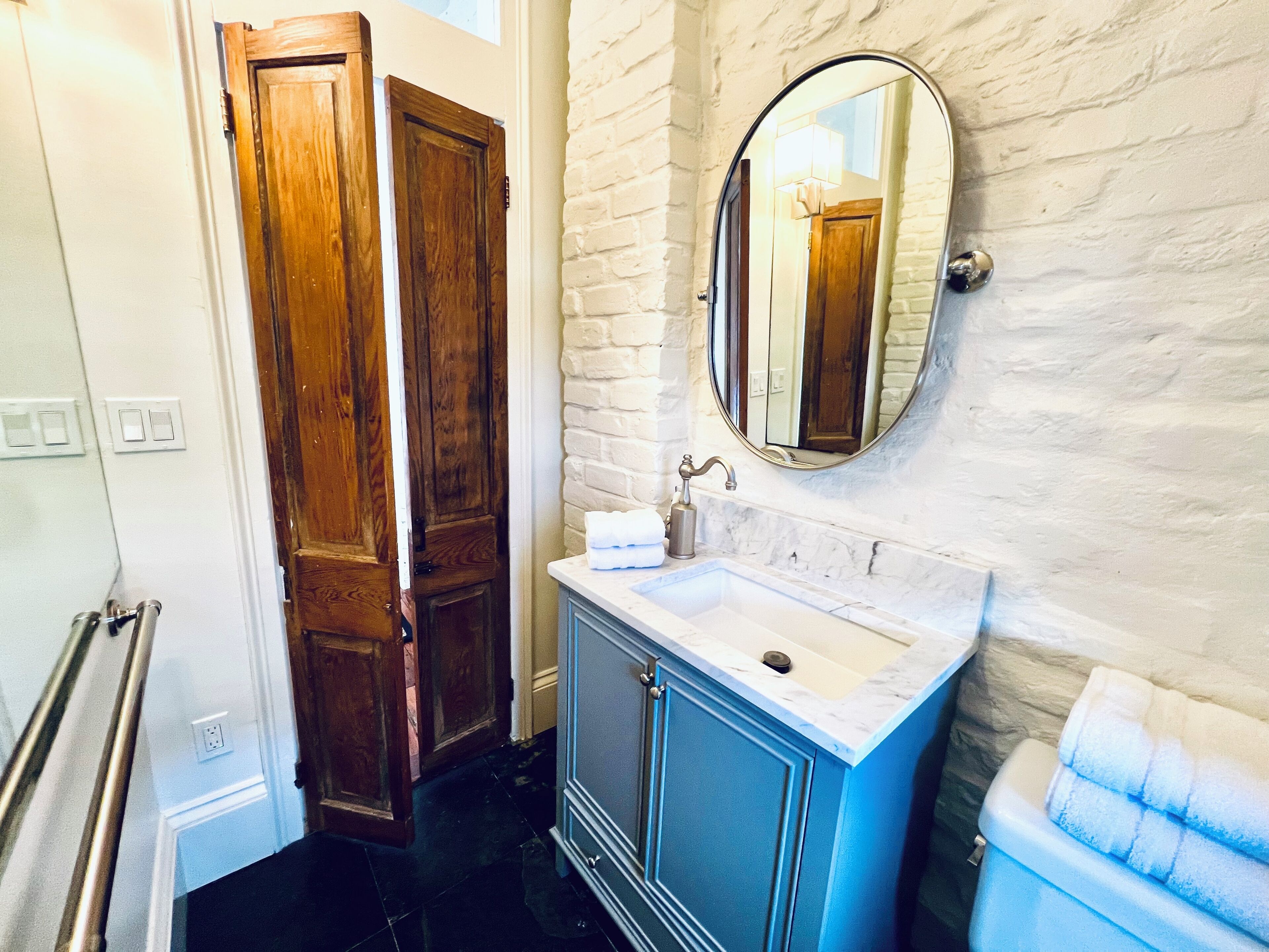 A bathroom with a wooden door, a sink with a marble countertop, a mirror, and a towel rack.