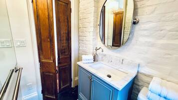 A bathroom with a wooden door, a sink with a marble countertop, a mirror, and a towel rack.